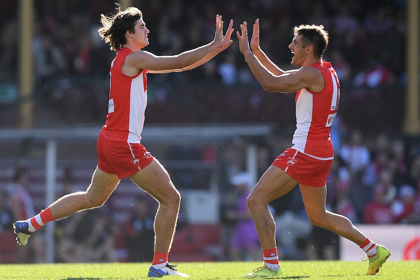 Two Sydney AFL players run towards each other to give two high fives after scoring a goal. 