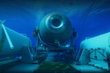A submersible vessel is seen underwater, attached to a larger platform