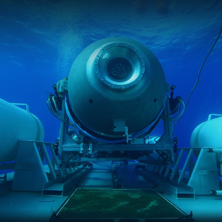 A submersible vessel is seen underwater, attached to a larger platform