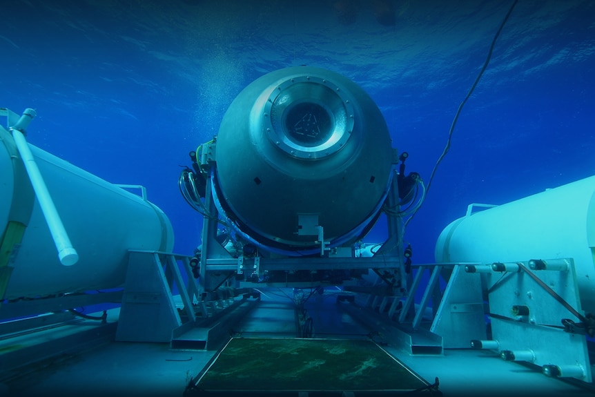 A submersible vessel is seen underwater, attached to a larger platform