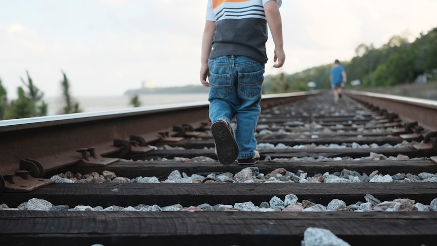 Young child walking with father along train tracks.