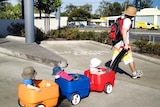 A father pulls his young triplets in a three cart carrier.