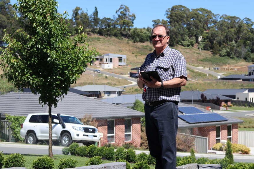 Chris Luck stands in front of houses with his tablet computer.