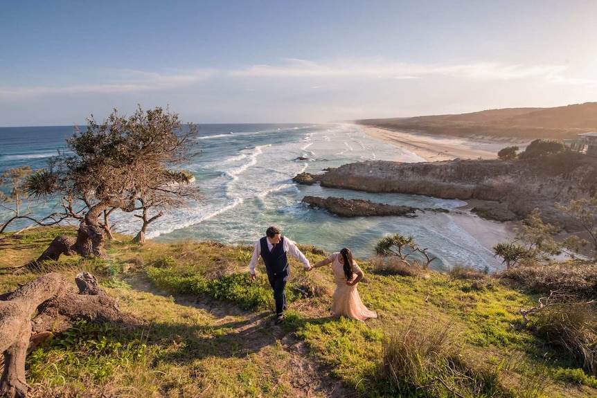 Couple Ruby and Matt walking up a hill above the ocean on their wedding day.