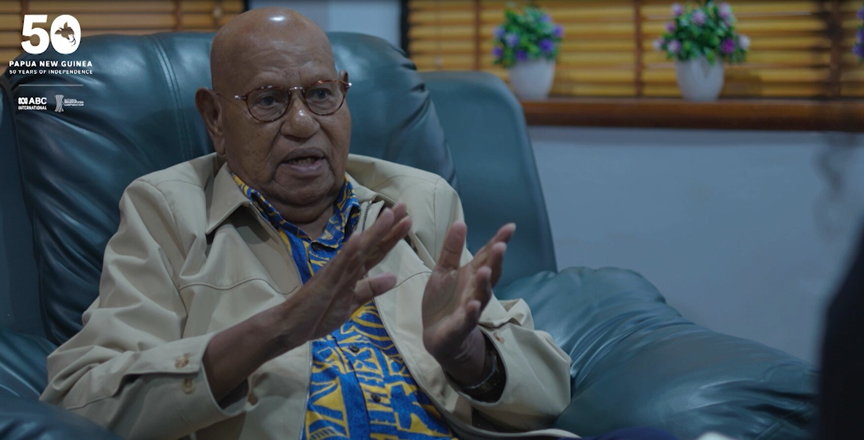  Dr John Momis wears cream jacket and sits on green chair. 