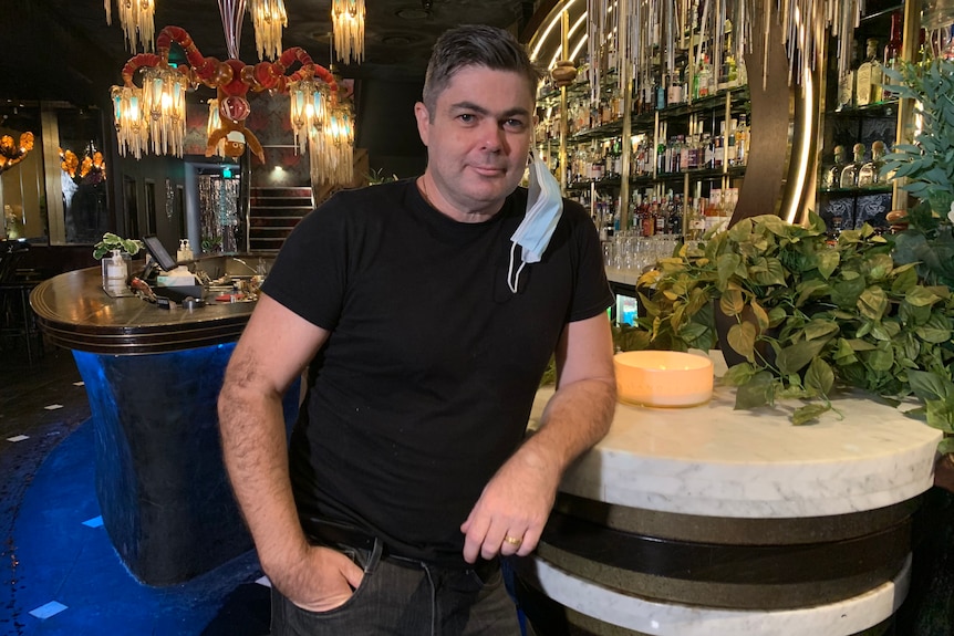 Geoffrey Slater leans on the bar at his business, with a face mask hanging on his ear.