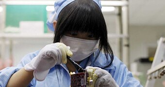 A woman wearing protective gear works with electronics in a lab environment.