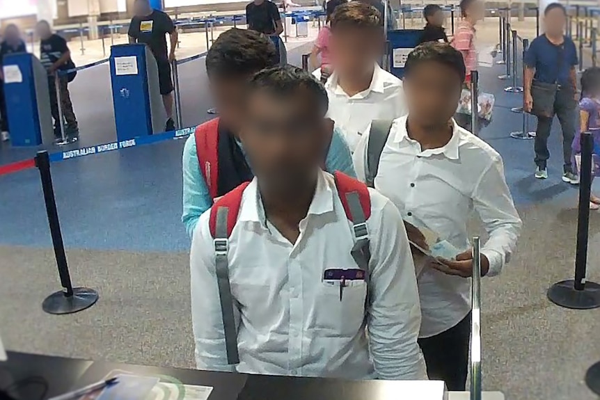 Four men, faces blurred, in an immigration queue at Brisbane Airport