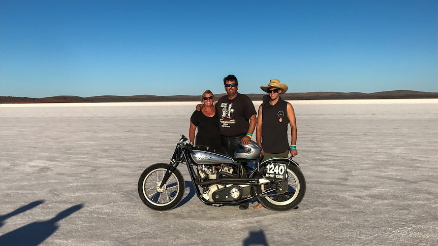 Peter Toni and Mason stand behind an Indian motorcycle on a salt plain.
