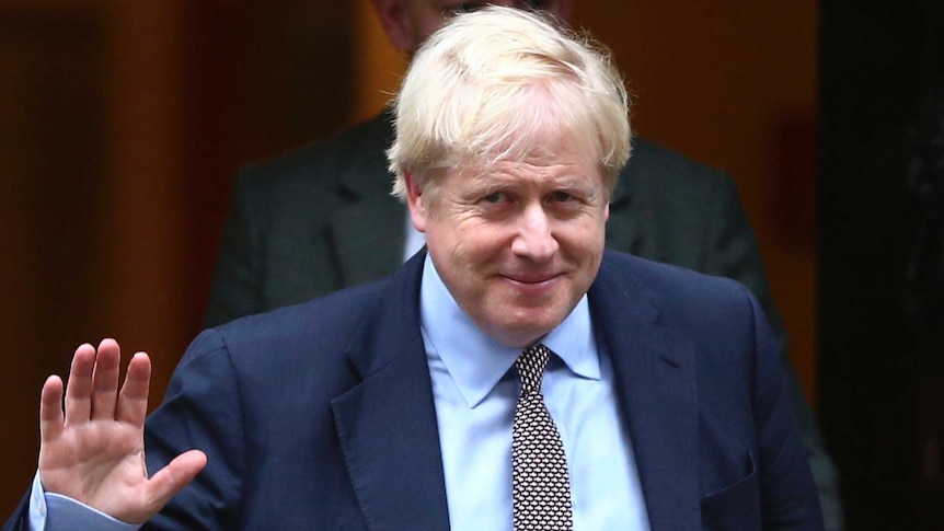 Boris Johnson holds up his hand in a wave and wears a blue suit