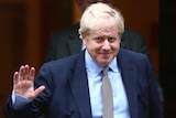 Boris Johnson holds up his hand in a wave and wears a blue suit
