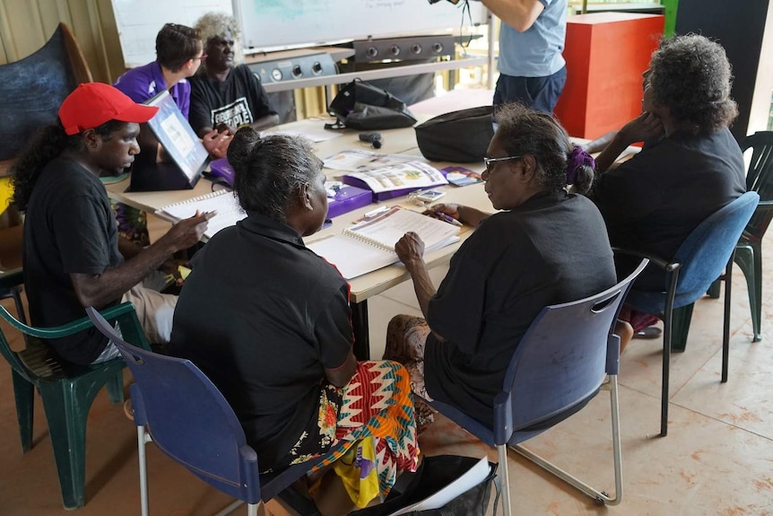 Voters sit around a table looking at enrolment pamphlets.