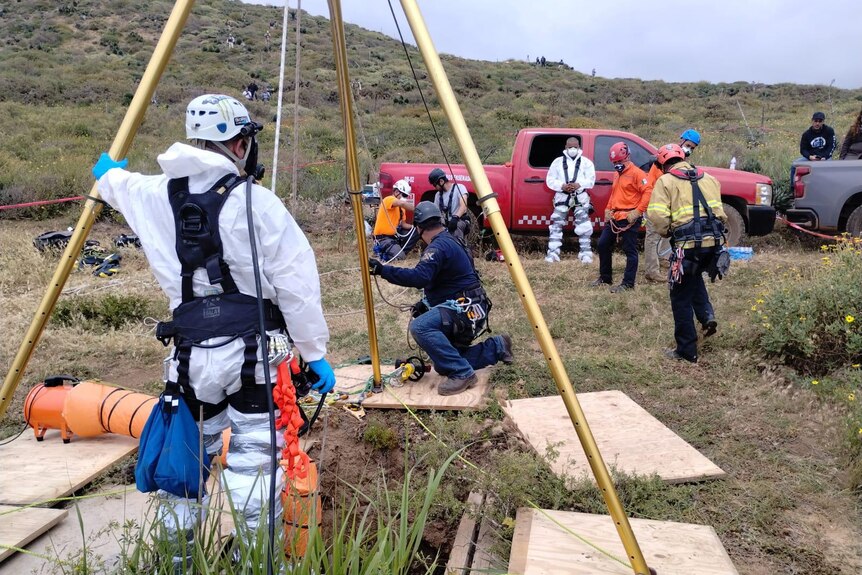Emergency workers in harnesses stand around a hole 