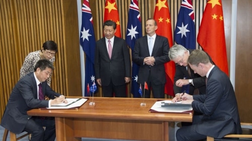 A group of people in front of Chinese and Australian flags with two signing documents.