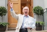 Ted McDermott stands on the stoop of Abbey Road Studios with his hands in the air and record in hand.