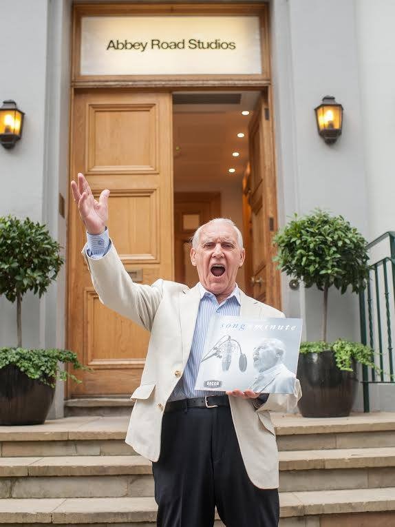 Ted McDermott stands on the stoop of Abbey Road Studios with his hands in the air and record in hand.