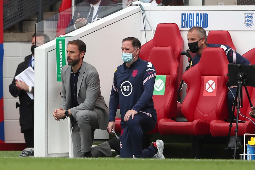 Three men take a knee on the sideline prior to the commencement of a football match