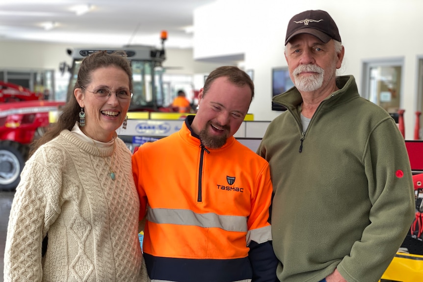 A man in a hi-vis vest stands between an older couple, his parents.