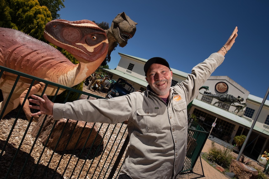 A man in a beige uniform jumps for joy outside the National Dinosaur Museum