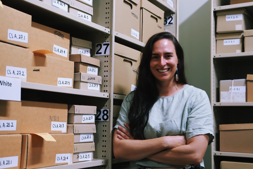 La mujer de pie frente a los estantes de cajas numeradas y sonriendo a la cámara