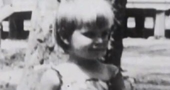 Black and white image of toddler with fair hair in front of tree