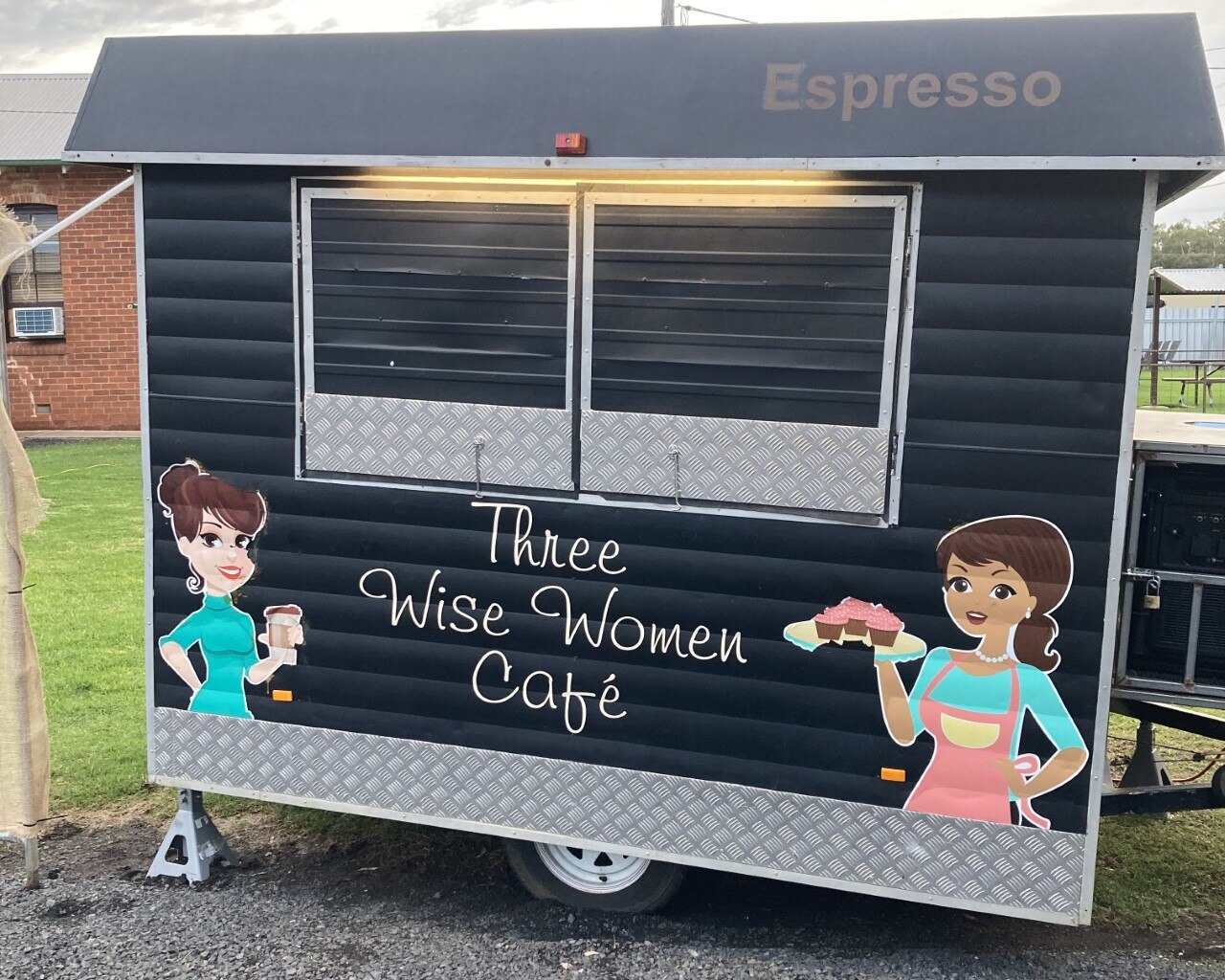 A black coffee van with the words "Cafe of the Three Sages" and paintings of two women holding coffee and cake.
