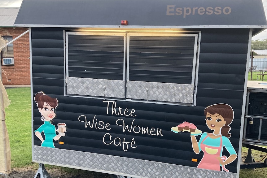 A black coffee van with the words "Three Wise Women Cafe" and paintings of two women holding coffee and cakes.