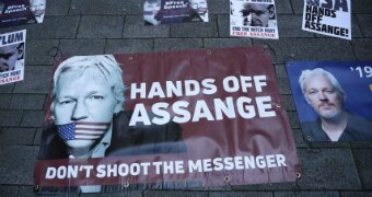 Posters on the ground with Assange on them, the centre-most has a picture of the US flag as a gag over his mouth.