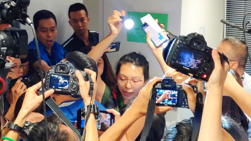 A woman with glasses is seen behind a throng of cameras she she holds up a flashlight to read a written statement.