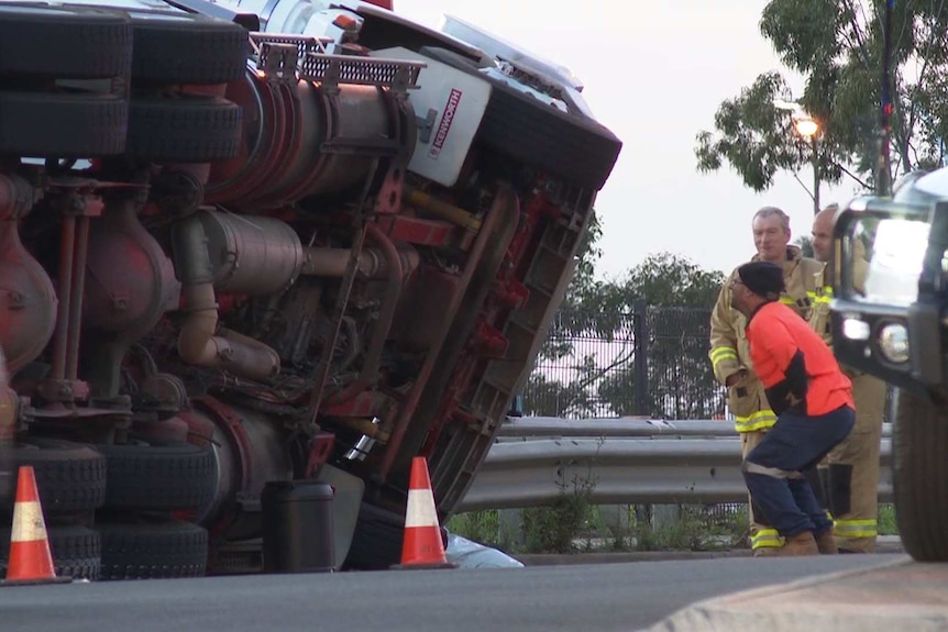 man looking at the underside of rolled over truck