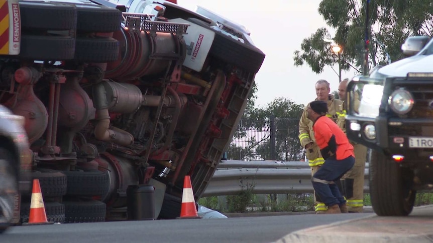 man looking at the underside of rolled over truck