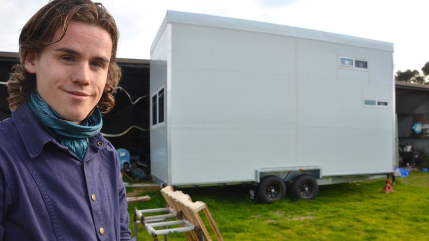 Person standing in front of a tiny house.