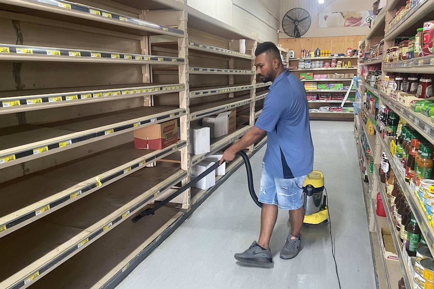 A man vacuums the empty shelves of a supermarket.
