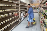 A man vacuums the empty shelves of a supermarket.