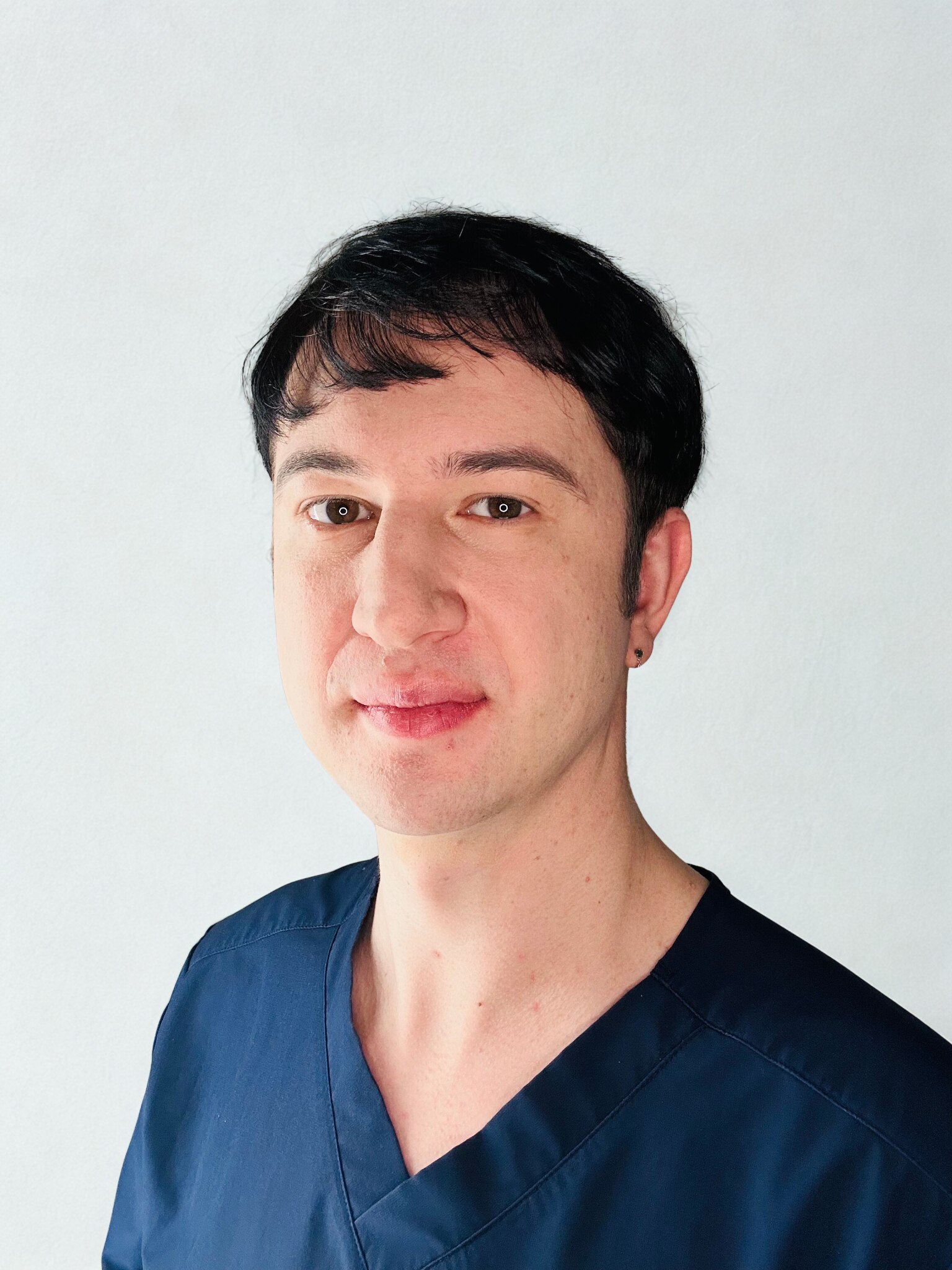 A young man with short brown hair wearing navy blue scrubs.