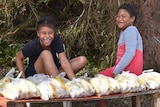 Two girls sit on a bench with bags of bananas.