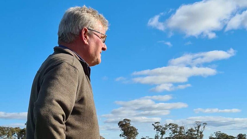 An older man with short, grey hair looks out across a rural property.