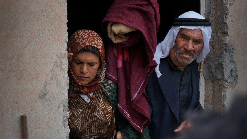 A group of Kurdish refugees look on from their doorway