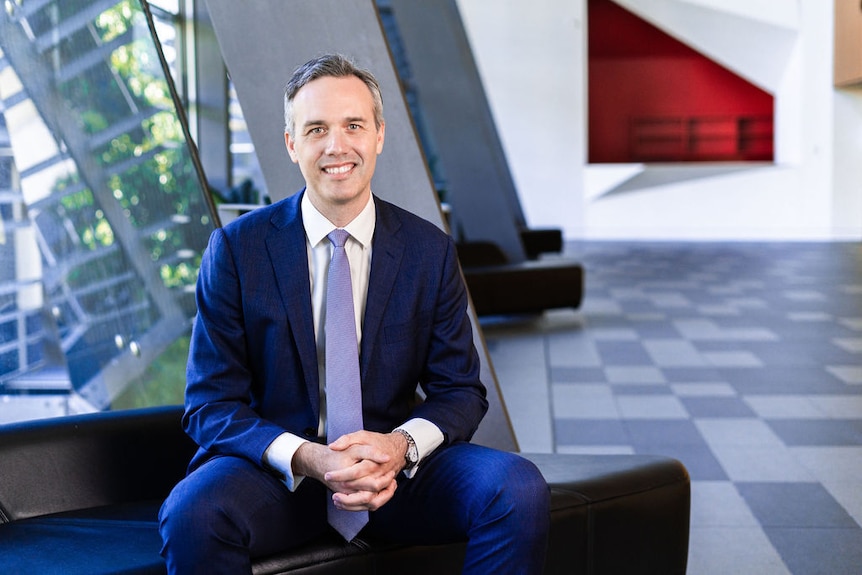 A portrait of a man in a suit sitting in a modern building lobby