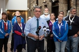 Gerard Hayes stands in a crowd in front of microphones.