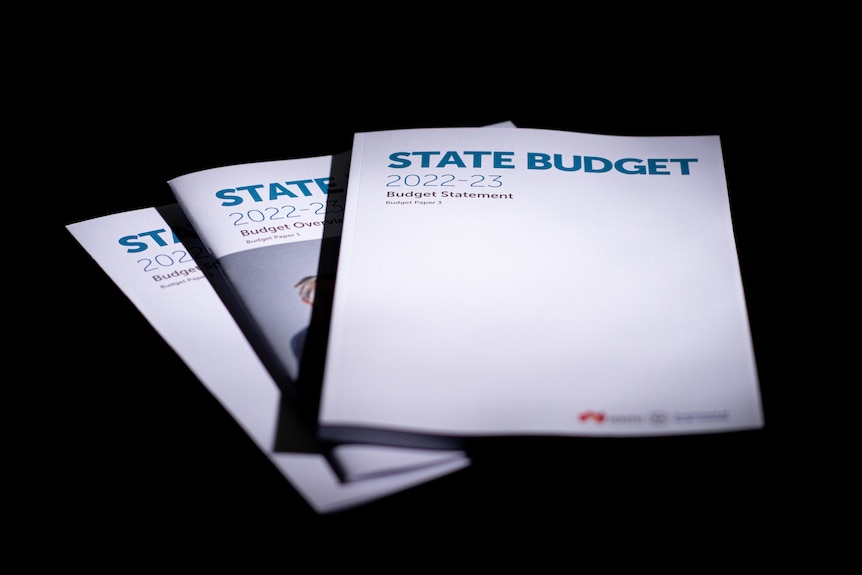 Three copies of the state budget papers fanned out on a black background