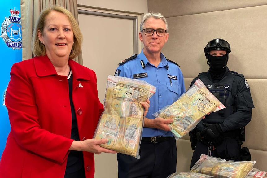 Police Minister Michelle Roberts and WA Police Acting Assistant Commissioner Allan Adams stand holding bags of cash.