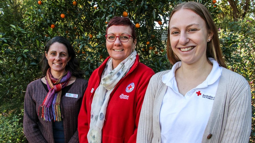 Three women stand facing the camera in a school garden