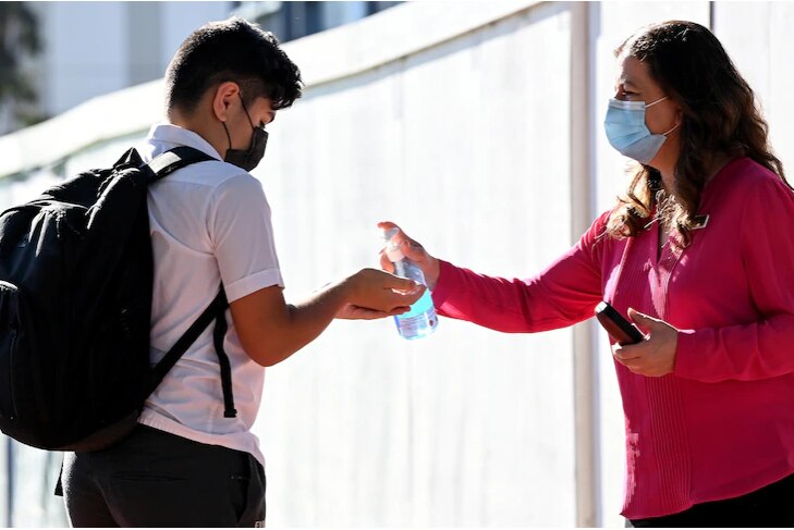 A woman in pink shirt is giving hand sanitiser to a student.