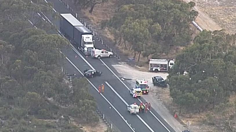 An aerial shot of a highway with a B-double truck, a black car, a black ute and emergency vehicles