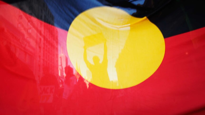 The shadows of protesters are seen through the fabric of an Aboriginal flag.
