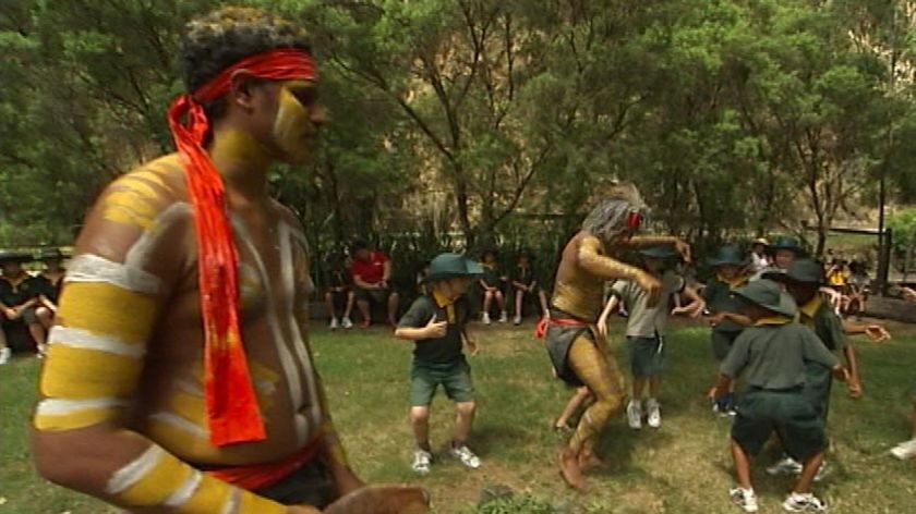 TV still of Indigenous dancers from the Nunukul Yuggera dance group performing with some school kids