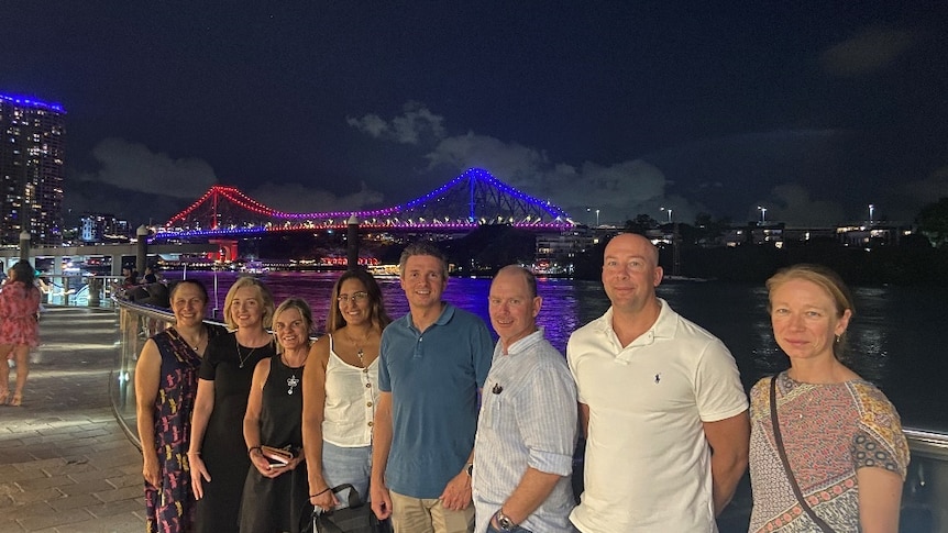 A group of people posing for a photo in front of a bridge lit up by coloured lights