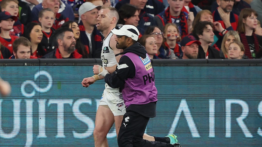 A Carlton AFL player grimaces as he is helped off the ground with a dislocated shoulder.