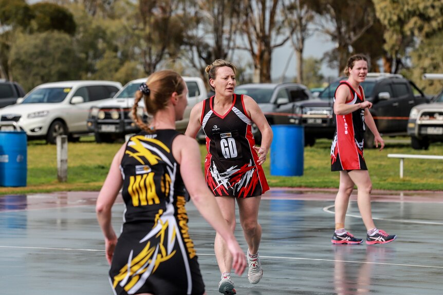 Woman running on netball court amid other players under grey skies
